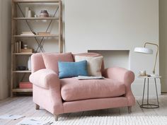 a pink chair sitting in front of a white wall with lots of pillows on it