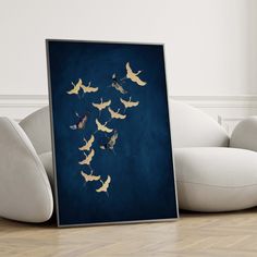 a framed photograph of birds flying in the air on a blue background with white furniture