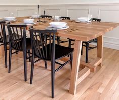 a wooden table with black chairs and white plates on it in a dining room setting