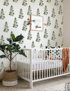 a white crib in front of a wall with trees on it