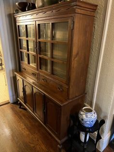 a wooden china cabinet sitting on top of a hard wood floor next to a wall