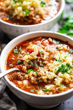 two white bowls filled with meat and vegetable soup on top of a gray table cloth