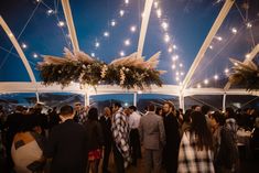 a group of people standing under a tent with fireworks in the sky behind them and onlookers