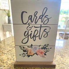 a sign that says cards and gifts with flowers on the front is sitting on a counter