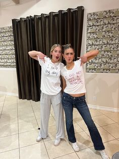 two young women standing in front of a mirror with their arms behind their backs, both wearing t - shirts that say sorry