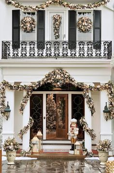 a white house decorated for christmas with wreaths on the front door and decorations hanging from the balconies