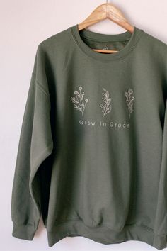 Grow in Grace A beautiful floral detail on a unisex crewneck sweatshirt. This makes a great gift for your flower loving friend! It's a great reminder that we all bloom and grow where we are nurtured and when we nurture ourselves. The cream embroidery on this military green sweatshirt brings a warm, comforting look just like mother nature herself! Specifications: 8 oz.(US) 13.3 oz.(CA), 50/50 preshrunk cotton/polyester Heather Sport colors: 60/40 polyester/cotton Air jet yarn = softer feel and re Floral Crewneck Sweatshirt, Embroidery Designs For Crewnecks, Cute Graphic Sweatshirt, Spring Crew Neck Sweatshirt, Spring Crew Neck Sweatshirt For Gift, Crew Neck Sweatshirt For Spring, Spring Relaxed Fit Sweater With Embroidered Graphics, Spring Cotton Sweatshirt Gift, Relaxed Fit Embroidered Sweater For Spring