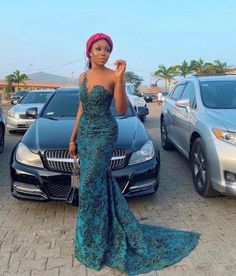 a woman in a blue dress standing next to some cars and posing for the camera