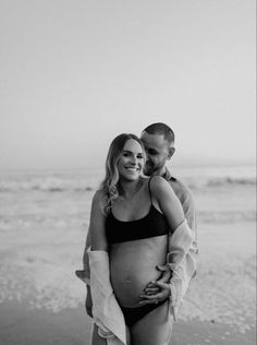 a pregnant woman is holding her husband on the beach