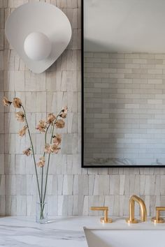 a vase with flowers sitting on top of a bathroom counter next to a mirror and sink