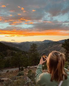 a woman is taking a photo with her cell phone at the top of a mountain