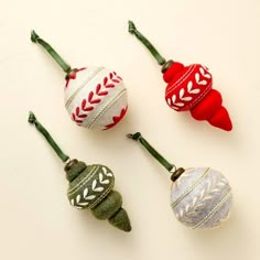 four ornaments are hanging from green stems on a white surface, one is red and the other is silver