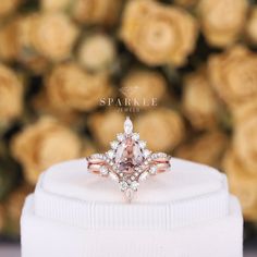 a pink diamond ring sitting on top of a white box with roses in the background