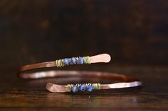 two thin copper and lapel bracelets with blue beads on the ends, sitting on a wooden surface