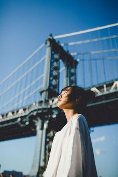 a man standing in front of a bridge looking up at the sky with his eyes closed