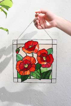 a hand holding up a stained glass window with red flowers on it and green leaves