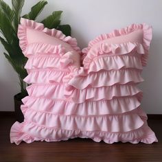 pink ruffled pillow sitting on top of a wooden floor next to a potted plant