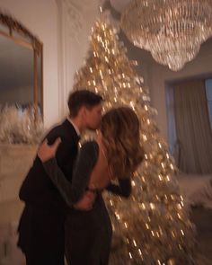 a man and woman kissing in front of a white christmas tree with lights on it