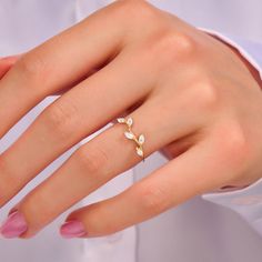 a woman's hand wearing a gold ring with two leaves on the middle of it