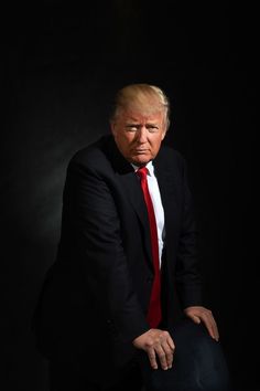 a man in a black suit and red tie posing for the camera with his hands on his knees