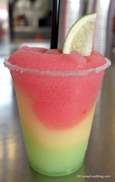 a close up of a drink with a slice of lime on the rim and watermelon