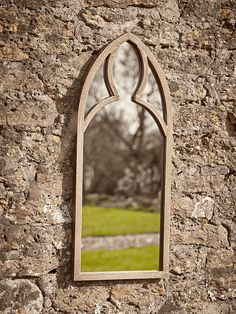 a stone wall with a mirror hanging on it's side and grass in the background