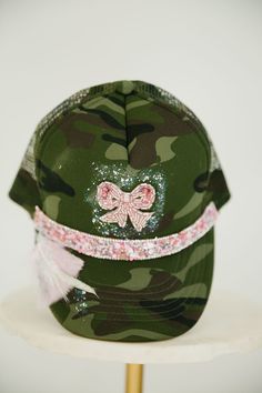 Make a fashion statement with this unique BEADED BOW CAMO TRUCKER HAT! Show off your style with the adjustable snapback and the camo pattern, pink beaded ribbon band, beaded bow patch, and a whole lotta' pink and white feathers with a hint of silver glitter. Get ready to turn heads! This is a made-to-order item. All customized orders are currently shipping within 14 business days. To receive item quicker, expedited shipping is available at checkout. Custom Baseball Hats, Beaded Ribbon, Camo Trucker Hat, Beaded Bow, Christmas Products, Hat Patches, Craft Show Ideas, Pink Beaded, White Feathers