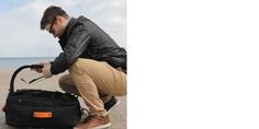 a man kneeling down next to a black bag on the beach with an orange handle