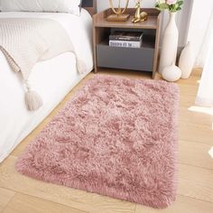 a pink rug on the floor next to a bed and nightstand with flowers in vases