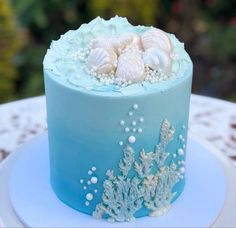 a blue and white cake with sea shells on it sitting on a platter in front of some flowers