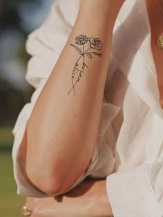 a woman with a flower tattoo on her arm, sitting in the grass and looking off into the distance