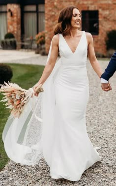 a bride and groom holding hands while walking down a gravel path in front of a brick building