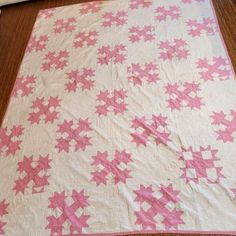 a pink and white quilt with stars on the top is laying on a wooden floor