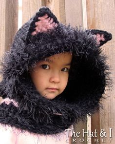 a young child wearing a black cat hat and scarf on top of a wooden fence