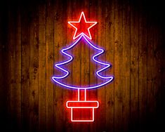 a neon christmas tree with a star on top is lit up against a wooden wall