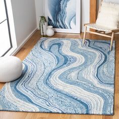 a living room area with a blue rug and white chair next to a painting on the wall