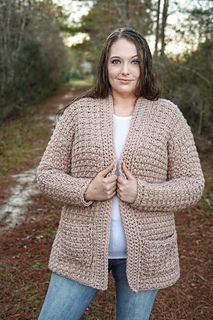 a woman standing in the middle of a forest wearing a cardigan sweater and jeans