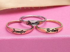 three personalized wedding rings sitting on top of a pink cloth covered table with the names of their bride and groom