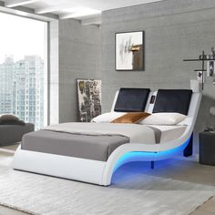 a white bed with blue lights on it in a room next to a large window