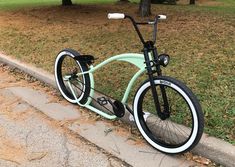 a mint green bicycle parked on the side of a road next to a tree and grass area