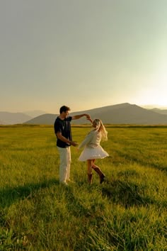 a man and woman standing in the middle of a field touching each other's hands