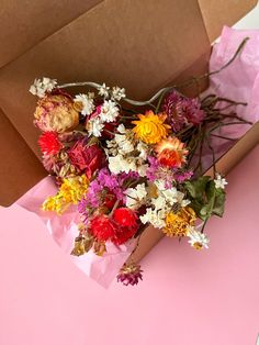 a bouquet of flowers sitting in a brown paper bag on a pink surface next to a cardboard box