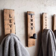 three wooden signs mounted to the side of a wall next to gray towels on hooks