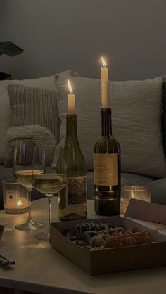 two bottles of wine are sitting on a table with food and candles in front of them