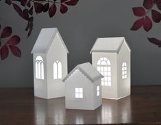 three white paper houses sitting on top of a wooden table next to red and green leaves