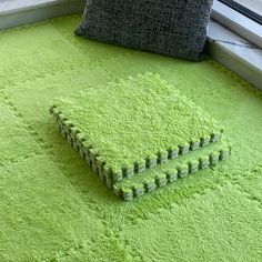 a bright green rug on the floor next to a window with a cushion and pillow