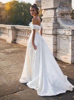 a woman in a white wedding dress standing on a bridge with her back to the camera