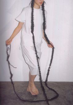 a woman with long black hair standing in front of a white wall