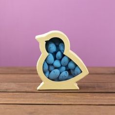 a small wooden bird with blue eggs in it's beak, on a table