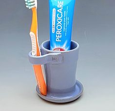 two toothbrushes are in a cup on a gray surface with an orange and blue toothpaste